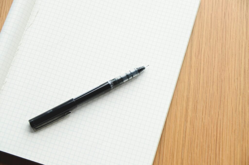 Jonass Bermttoni Black pen resting on an open grid notebook, perfect for writing or design.