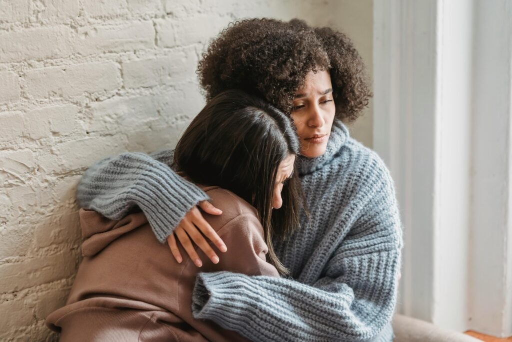 Two friends share an emotional embrace, offering comfort and support indoors.