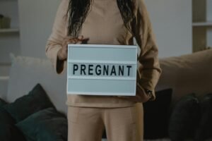 A woman in beige holds a lightbox with 'PREGNANT' indoors. Expectant motherhood concept.